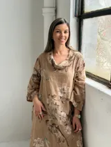 Vestido largo de lino color camel con estampado floral en tonos marrón y crudo, cuello drapeado y mangas largas holgadas.