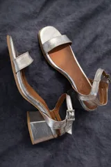 Sandalias de cuero color dorado, con taco cuadrado y tira delgada en el tobillo.