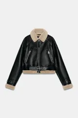 Cazadora de estilo aviador con exterior de cuero sintético negro y forro interior de piel sintética en tono beige. Presenta cuello solapa, cierre frontal con cremallera, bolsillos laterales con cremallera, trabillas en los puños y cinturón ajustable en el bajo con hebilla metálica.