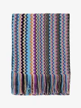 Chal o bufanda de tejido de punto con patrón zigzag (chevron) multicolor, predominando tonos azules, morados, naranjas y negros. Presenta flecos en los bordes.