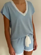 Pijama celeste de algodón acanalado compuesto por una remera de manga corta con escote en V adornado con puntilla blanca, y un short a juego con elástico y lazo de ajuste en la cintura.