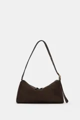 Bolso de hombro de diseño estructurado en color marrón, confeccionado en material tipo gamuza. Presenta un asa larga trenzada ajustable con hebilla metálica dorada y cierre superior con cremallera.