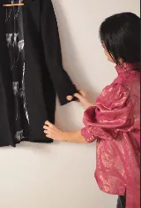 Blusa de lino color salmón con cuello alto, mangas abullonadas y detalle de alforzas en el frente. Presenta terminaciones con puntilla ondulada negra y cierre posterior con botones a la vista.