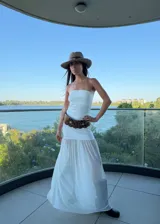 Vestido largo blanco de silueta fluida con escote strapless y falda de caída liviana con efecto translúcido.