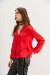 Camisa roja de manga larga con cuello redondo y escote frontal con botones ocultos. Presenta detalles de alforzas y frunces en los hombros.