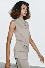 Top de algodón color beige con cuello recto, mangas asimétricas y detalle de tejido drapeado en el frente.