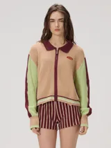 Campera estilo bomber de tejido de punto con diseño colorblock en tonos tostado, verde y bordó. Cuenta con cuello camisero, cierre frontal completo y un parche gráfico bordado en el pecho.