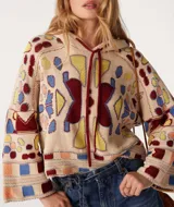 Sweater de punto beige con capucha y cordones burdeos. Presenta un diseño jacquard con motivos geométricos en azul, amarillo y rojo.