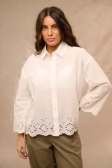 Camisa blanca de manga larga con diseño oversize, cuello camisero y cierre frontal de botones. Presenta detalles de bordado inglés calado en el ruedo y en los puños acampanados.