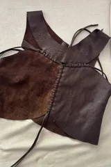Top de cuero ovino en tonos chocolate y distress, con diseño de paneles combinados y detalles de costuras en pasamanería. Presenta un corte asimétrico con tiras para atar.