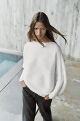 Sweater de punto blanco con textura acanalada horizontal, cuello barco, mangas largas amplias y corte holgado.