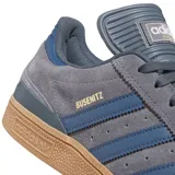 Championes Adidas Busenitz de skate, color gris oscuro con tres franjas laterales en azul marino y detalles en dorado. Suela de goma color caramelo.