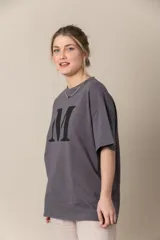 Remera gris con estampa de la letra M en negro y cadena plateada en el cuello.