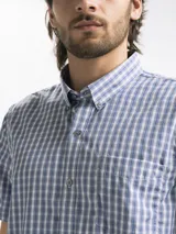 Camisa de hombre de manga corta con estampado a cuadros en tonos blanco, verde y marrón. Tiene cuello abotonado y bolsillo en el pecho.