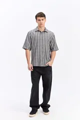 Camisa de manga corta oversize en tejido rústico, con diseño de rayas verticales celestes y blancas, cuello clásico y cierre frontal de botones.