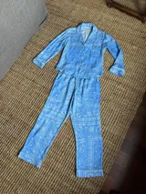 Pijama de algodón con estampado abstracto en tonos celestes, violetas y verde oliva, compuesto por una camisa de manga larga con botones y cuello solapa, y un pantalón largo de corte recto con elástico en la cintura.