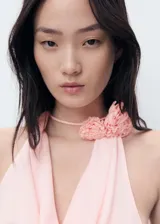 Blusa sin mangas color rosado, con cuello drapeado y detalle de flor aplicada en el cuello. Presenta un diseño recto y holgado.