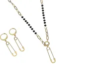 Set de collar y caravanas de acero con baño de oro y cristales negros. El collar tiene un dije de alfiler y las caravanas también tienen forma de alfiler.