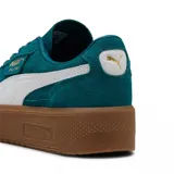 Championes Puma modelo Palermo Elevata, de diseño urbano con plataforma. Presenta una capellada de gamuza negra con la icónica franja lateral en cuero blanco y detalles dorados en la lengüeta y el lateral. Cuenta con una suela de plataforma de goma color caramelo.