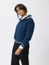 Sweater de tejido grueso en color beige, con cuello alto y cierre frontal parcial. Presenta detalles de rayas negras en contraste en el borde del cuello y en los puños.
