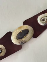 Cinto tipo faja de cuero color marrón chocolate, con apliques metálicos grabados de formas geométricas y piedras oscuras incrustadas.