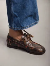 Mocasines de cuero color marrón óxido con cordones y costuras pespunteadas en rojo.