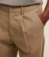 Pantalón de sastrería color beige, de corte holgado y diseño loose, con pliegues frontales, bolsillos laterales y cierre tradicional.