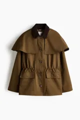 Chaqueta de sarga color marrón con cuello de pana de algodón oscura, capa decorativa desmontable, cierre de botones delanteros, bolsillos con solapa y cordón interior para ajustar la cintura.