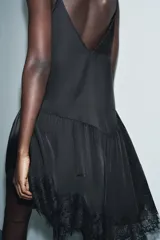 Top negro de tirantes finos con escote pico. Presenta bordados ornamentales en el frente y detalles de puntilla en el escote y el bajo asimétrico.
