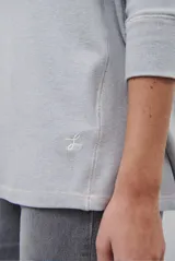 Remera de manga larga en color beige, confeccionada en tejido de punto con costuras a la vista en contraste. Presenta un corte holgado, cuello redondo y un pequeño bordado distintivo en la parte inferior.