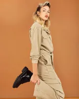 Botinetas de caña baja con suela track gruesa, combinando cuero negro en la puntera, gamuza marrón en el lateral y detalles de textura animal print tipo serpiente en tonos marrones. Presenta un cierre de solapa con velcro en el empeine.