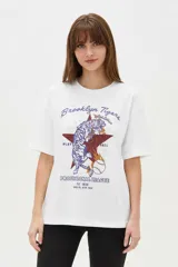 Remera de algodón negra de manga corta y cuello redondo, con estampa frontal que incluye letras rojas y gráficos en tonos dorados.
