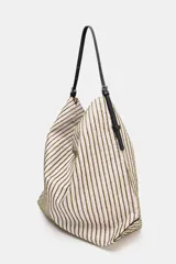 Bolso tipo shopper de tejido con diseño de cuadros en tonos verdes, blancos y marrones, decorado con apliques brillantes. Cuenta con asa de hombro ajustable en material sintético negro, cierre mediante botón imantado y bolsillo interior con cremallera.