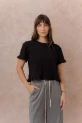 Remera blanca de corte crop y calce relajado, con cuello redondo y mangas corta terminadas con delicados volados, al igual que el ruedo.