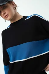 Buzo de punto con diseño de franjas horizontales en azul y blanco sobre fondo negro. Presenta cuello redondo, mangas caídas con puños elastizados y un corte holgado.