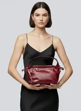 Bolso de hombro color borgoña (Syrah) con efecto cuero y acabado arrugado. Presenta un cierre fruncido en la parte superior y una correa ajustable para llevar al hombro.
