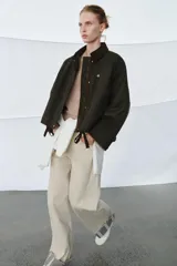 Chaqueta encerada de corte oversize, color marrón oscuro, con cuello de pana en contraste. Presenta cierre frontal con cremallera y botones a presión ocultos bajo solapa, bolsillos delanteros y mangas largas con puños ajustables.