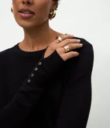 Suéter de punto ajustado con cuello redondo y manga larga. Presenta detalle de botones metalizados en los puños.