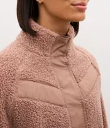 Campera bomber de mujer confeccionada en tejido sherpa color rosa viejo, con cuello alto, cierre frontal con cremallera y detalles de paneles lisos contrastantes en el pecho.