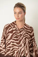 Camisa de manga larga con cuello camisero, corte holgado y estampado de cebra en tonos marrón y negro. Presenta una guarda horizontal con efecto esfumado en negro y marrón en el bajo y puños.
