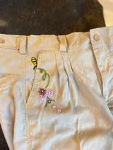 Bombacha de lino color beige con delicado bordado artesanal de flores y una abeja cerca de uno de los bolsillos.