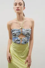 Vestido largo con diseño bicolor, cuerpo superior estampado con aberturas y hebillas metálicas, y falda inferior de satén en color verde lima. Presenta escote halter con cordones para anudar al cuello.