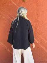 Capa corta de textura tipo bucle en color negro, con cuello alto, cierre frontal de botones y mangas tres cuartos con corte raglán y silueta en A.