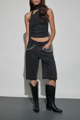 Bermuda de denim negro con diseño holgado, tiro medio y detalles de tachas y strass aplicados en los bolsillos delanteros. Presenta terminaciones deshilachadas en las piernas.