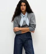 Suéter de punto gris con escote en V y detalle de camisa integrada en color celeste a rayas, con cuello estructurado y lazo frontal. Diseño de corte regular y mangas largas.