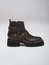Bota corta de cuero con efecto desgastado, color marrón oscuro. Presenta dos correas con hebillas metálicas decorativas y suela de goma negra con plataforma dentada.