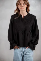 Camisa negra de corte holgado con detalles de bordado tipo broderie en el pecho y mangas largas con puños acampanados.