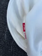 Hoodie de color blanco off-white con diseño de capucha, bolsillo frontal tipo canguro y bordado en relieve con el texto ITTAI STARS y un logo caligráfico.