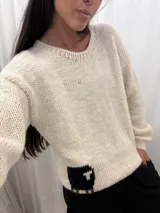 Buzo tejido a mano en lana merino, color crudo, con diseño de una oveja negra en la parte inferior trasera. Presenta cuello redondo, mangas largas y corte holgado.