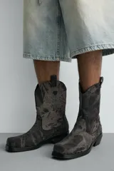 Bota estilo cowboy fabricada en tejido denim de algodón con efecto lavado, diseño de caña media con tiradores laterales, horma cuadrada y tacón ancho.